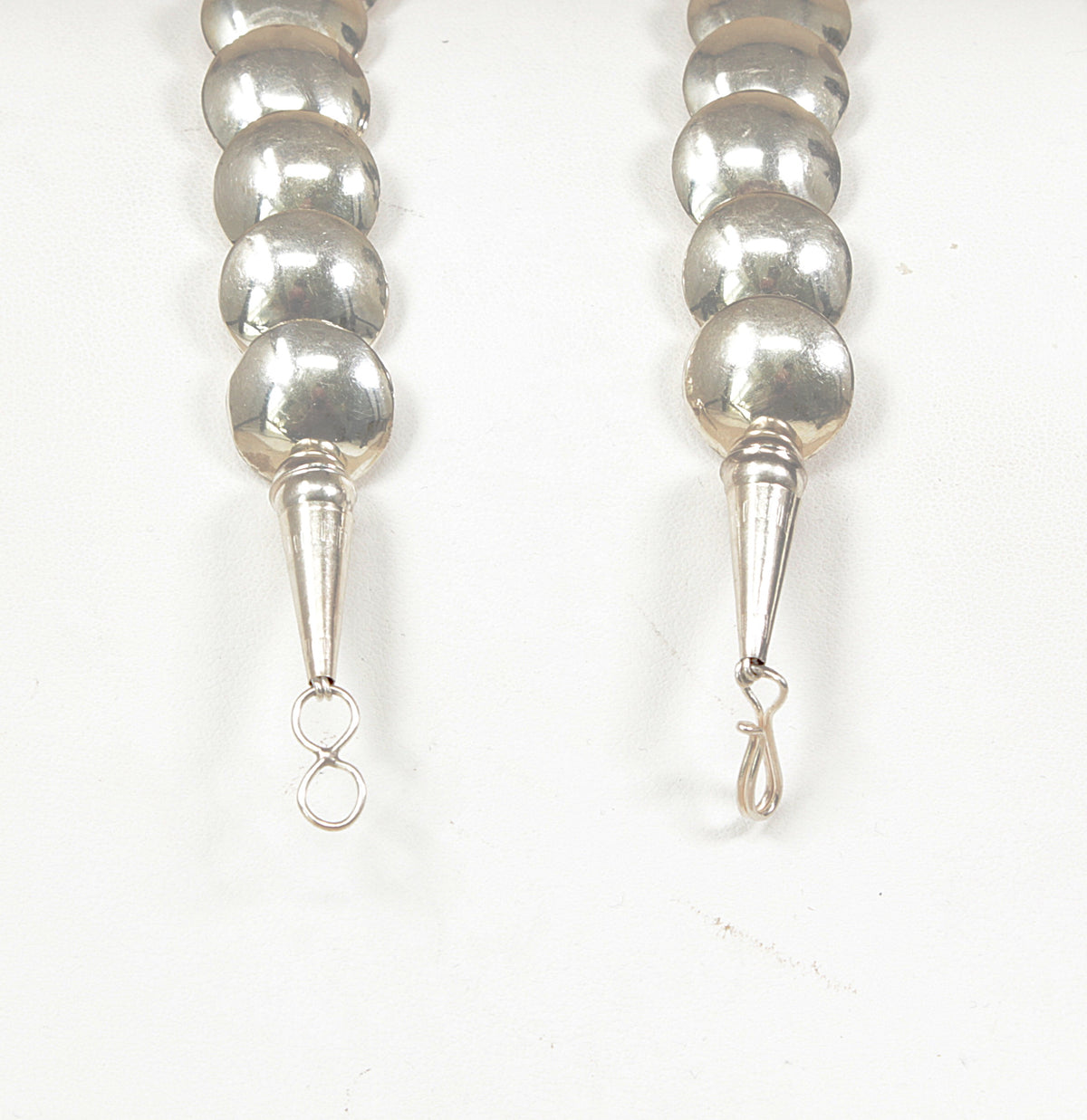 Close-up of the lower ends of two silver beaded strands, showing metallic round beads, tapered silver accents, and small hanging loops on a plain white background.