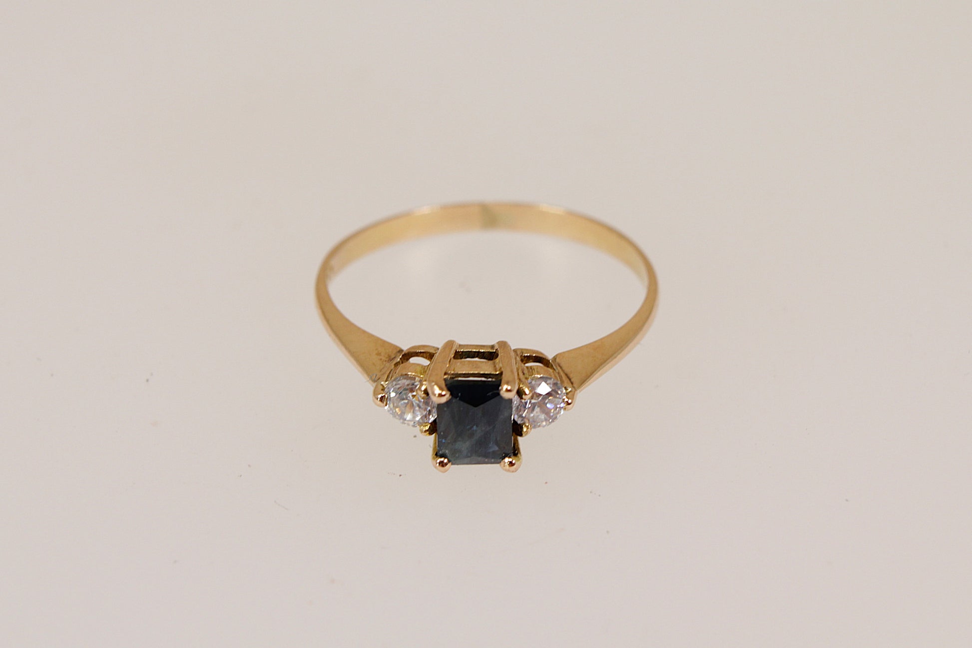 Gold ring with a central blue sapphire  gemstone and two smaller cubic zirconia diamond simulant gemstones  on a light gray background