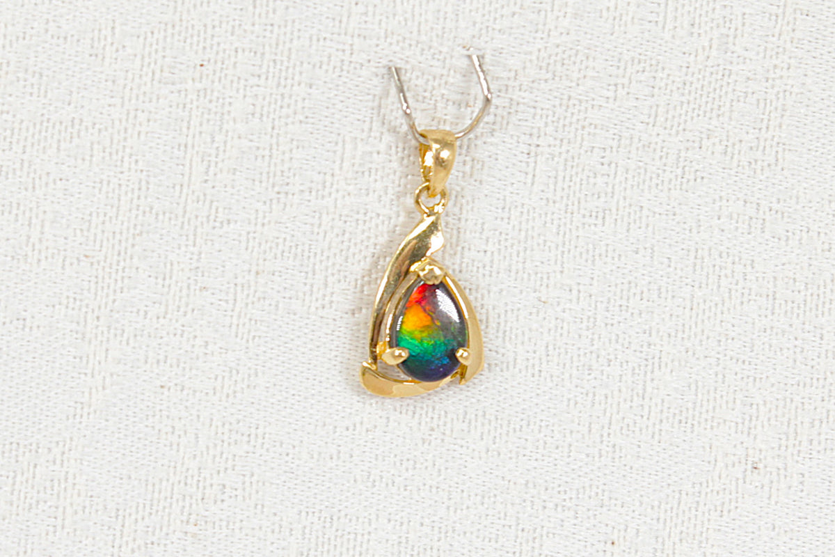 A gold pendant featuring a teardrop-shaped iridescent labradorite  gemstone, displayed on a textured white fabric background.