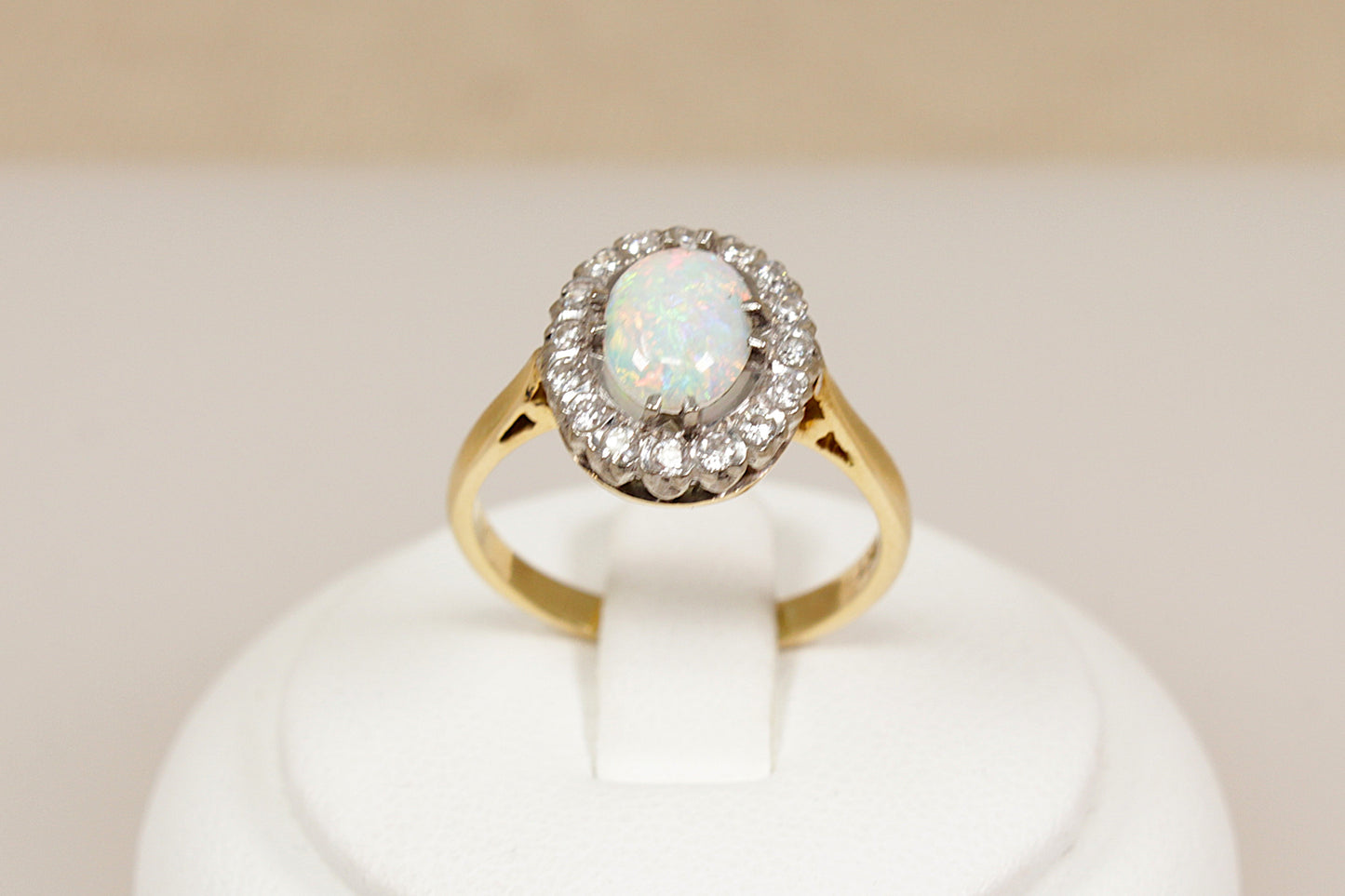 18ct gold ring with central opal gemstone surrounded by halo of  diamonds on a white stand