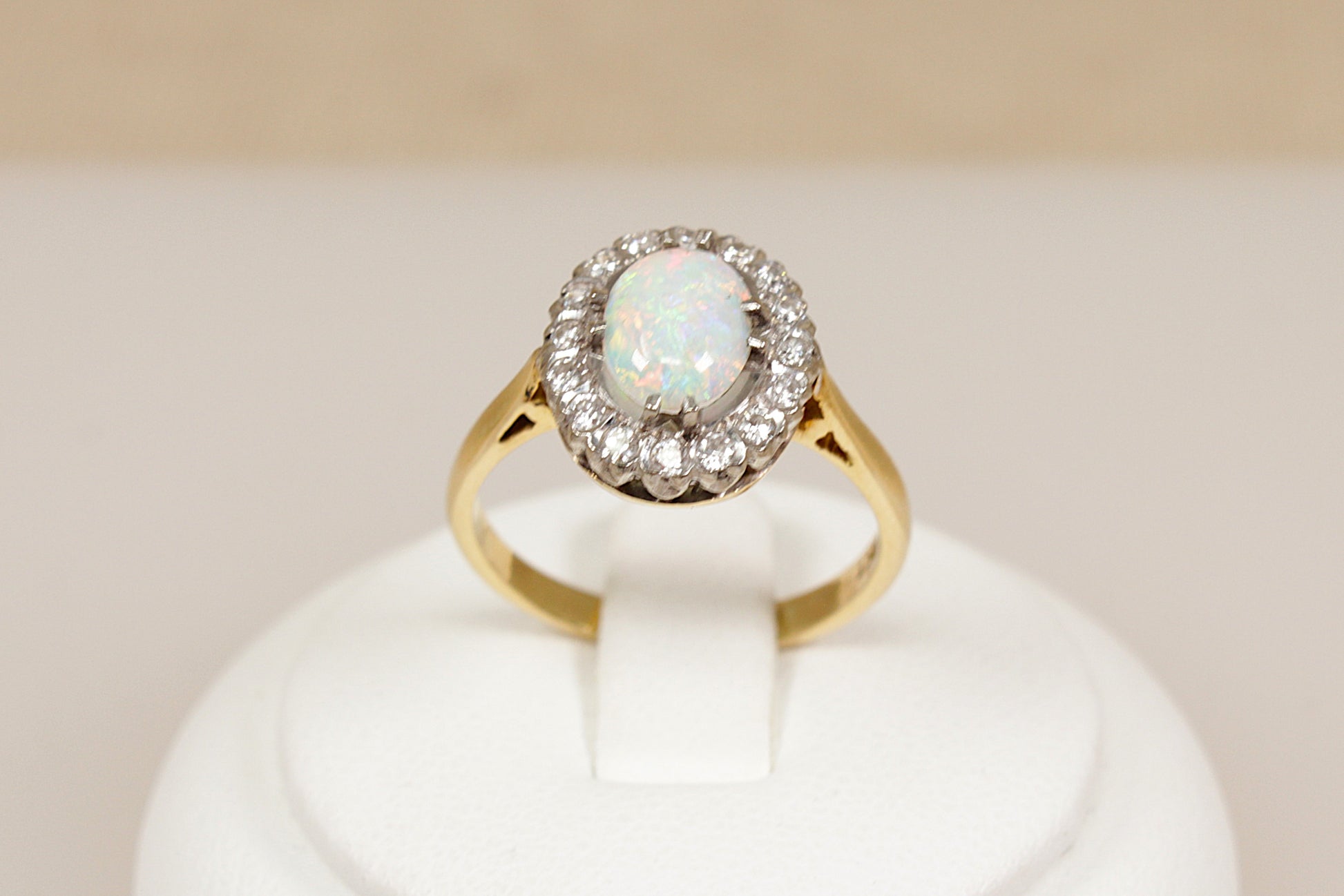 18ct gold ring with central opal gemstone surrounded by halo of  diamonds on a white stand