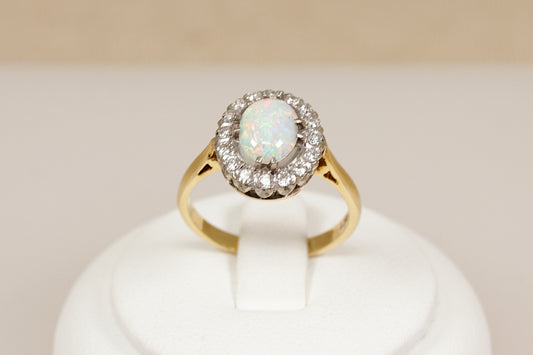 18ct gold ring with central opal gemstone surrounded by halo of  diamonds on a white stand