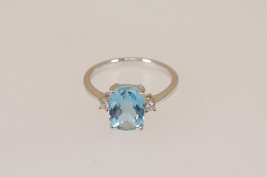 White 18ct gold ring with a blue topaz and white diamond gemstones on a light beige background
