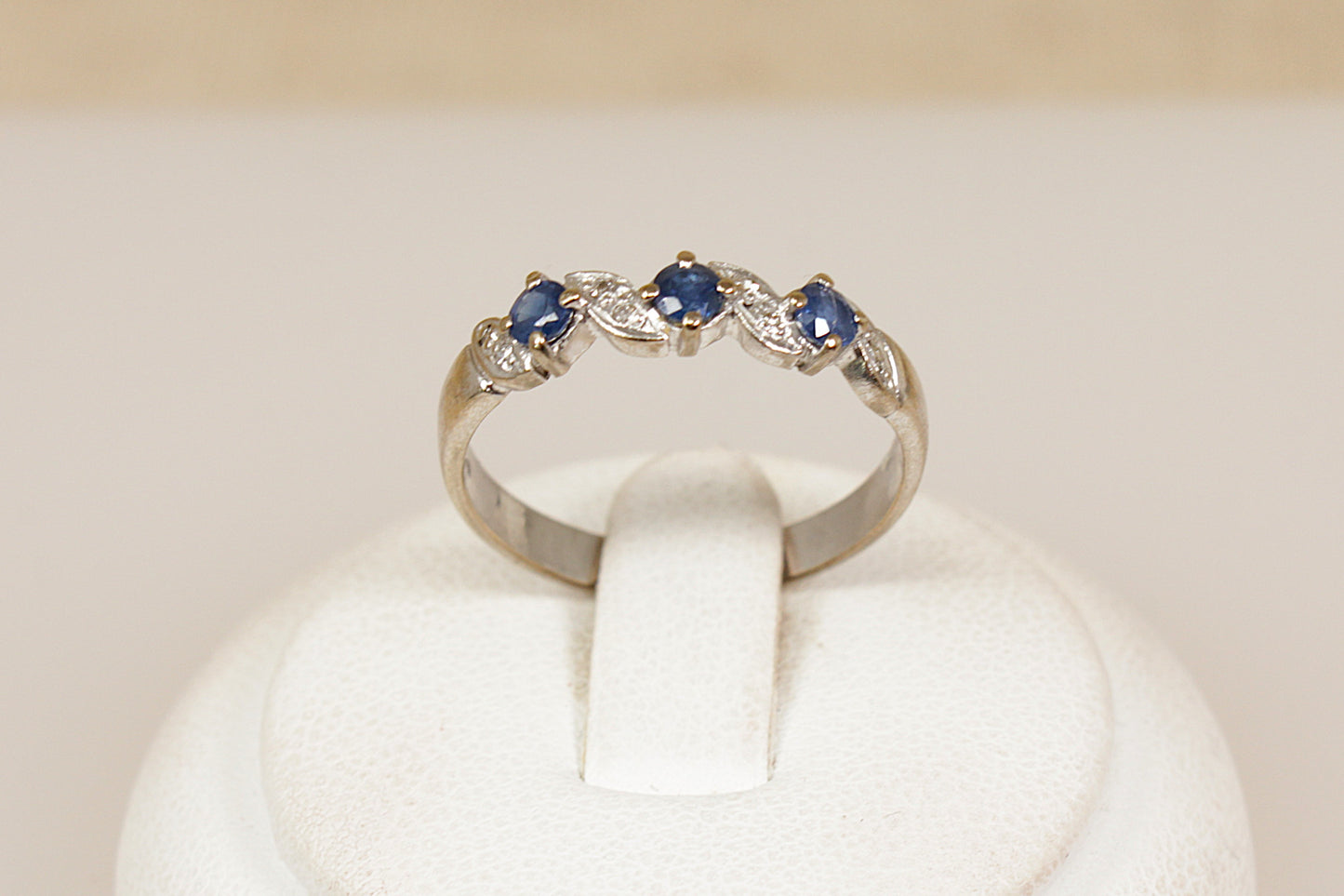 18ct white gold ring with three faceted  blue sapphire with diamond accents on a white stand