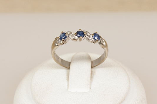 18ct white gold ring with three faceted  blue sapphire with diamond accents on a white stand