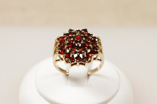 A 9ct gold garnet cluster ring with multiple garnet stones arranged in a circular pattern in the center, displayed on a white mount.