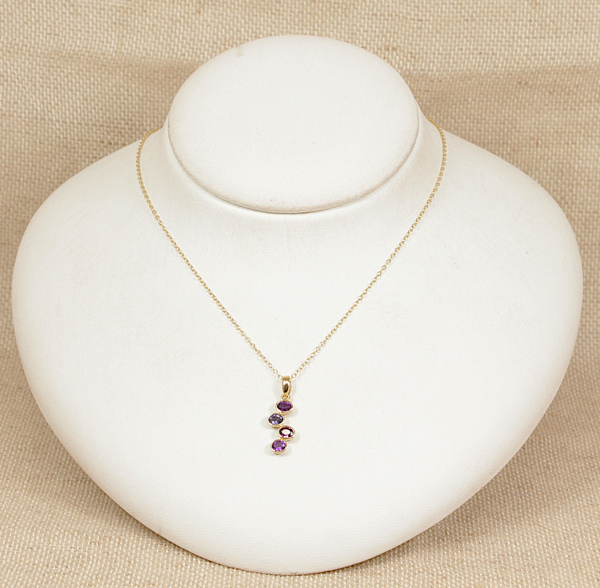 Gold necklace with amethyst garnet blue iolite gemstones on a white mannequin bust against a beige background