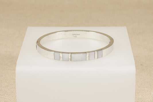 Silver bracelet with a mother of pearl inlay on a white cube against a beige background