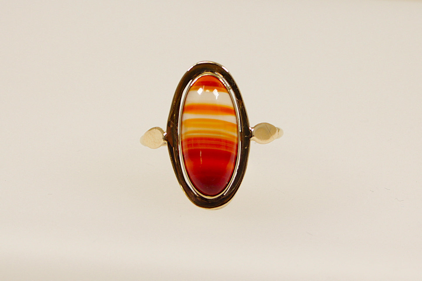 An oval-shaped banded carnelian stone set in a gold ring with the stone displaying reddish-orange hues. The gold band is uncomplicated and elegant, the band is stamped on the outside 333 for 8ct gold, the warm tones of the yellow gold complement the deep colour of the carnelian, creating a harmonious and eye-catching piece. This ring is often associated with vintage or antique styles with a modern twist. UK finger size Q.