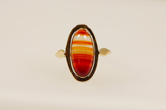 An oval-shaped banded carnelian stone set in a gold ring with the stone displaying reddish-orange hues. The gold band is uncomplicated and elegant, the band is stamped on the outside 333 for 8ct gold, the warm tones of the yellow gold complement the deep colour of the carnelian, creating a harmonious and eye-catching piece. This ring is often associated with vintage or antique styles with a modern twist. UK finger size Q.