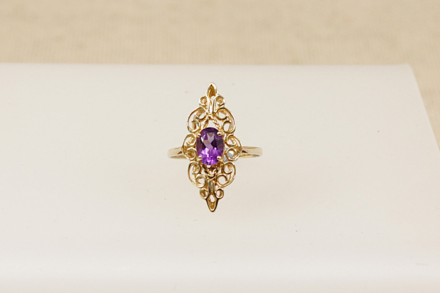 A 9ct gold ornate navette-shaped ring with a deep purple oval Amethyst gemstone on a white background.