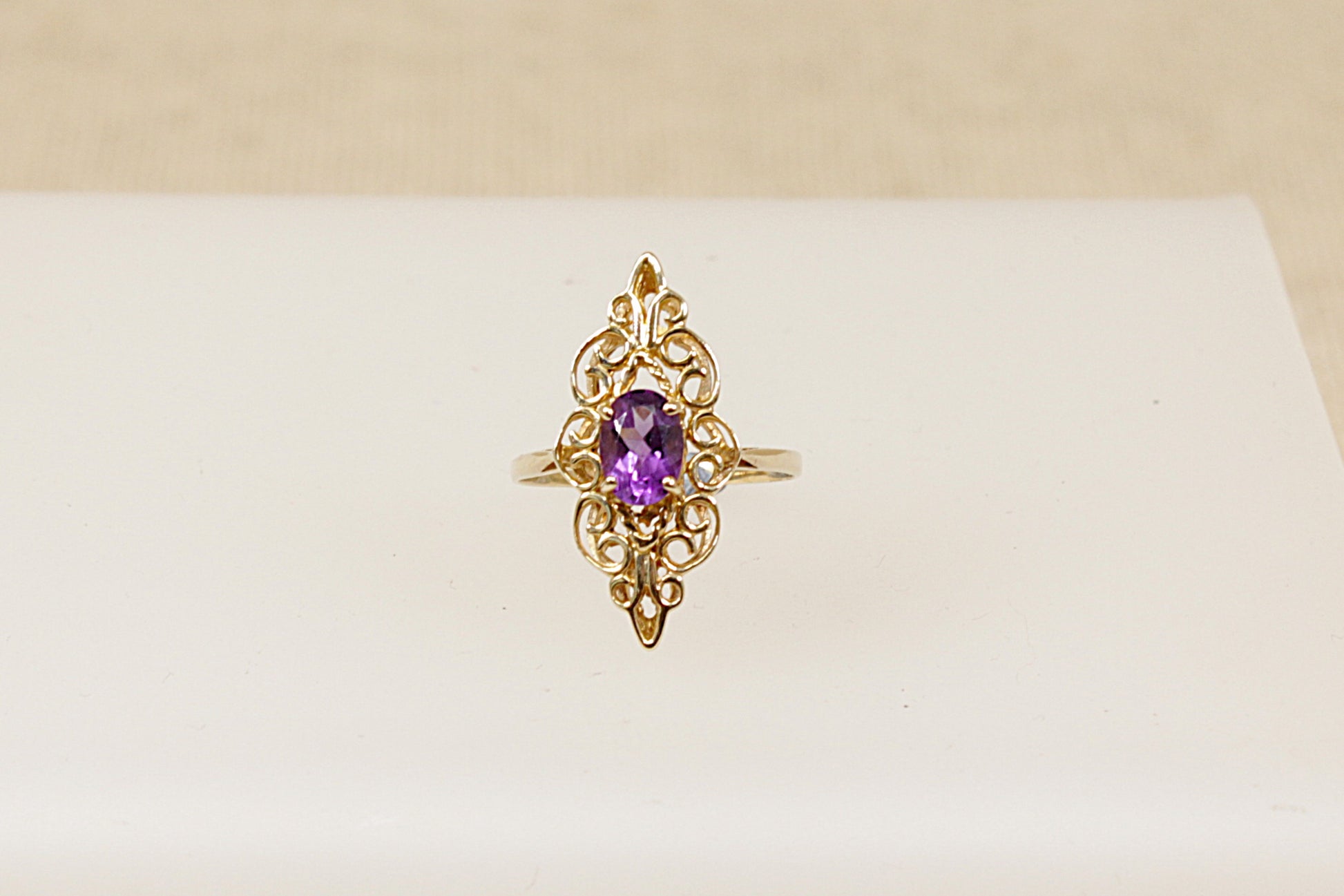 A 9ct gold ornate navette-shaped ring with a deep purple oval Amethyst gemstone on a white background.