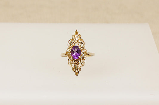A 9ct gold ornate navette-shaped ring with a deep purple oval Amethyst gemstone on a white background.