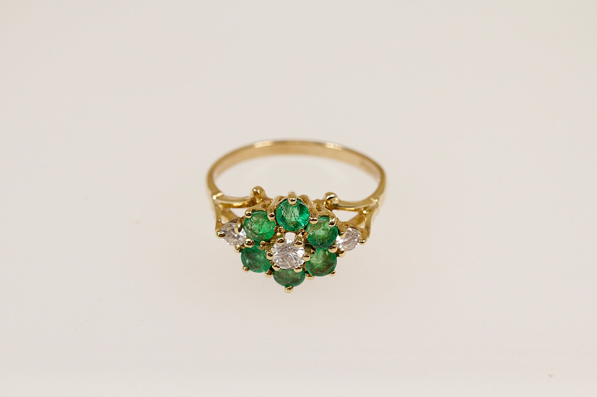 A vintage 9ct gold emerald and diamond cluster ring with a floral design, featuring a central cluster of green emeralds surrounded by white diamonds.