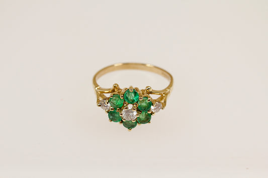 A vintage 9ct gold emerald and diamond cluster ring with a floral design, featuring a central cluster of green emeralds surrounded by white diamonds.