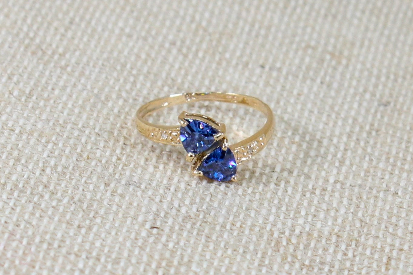 This stunning ring has 2 trillion cut Blue Iolite gemstone. On the shoulders are clear Cubic Zirconia on a beige background. 