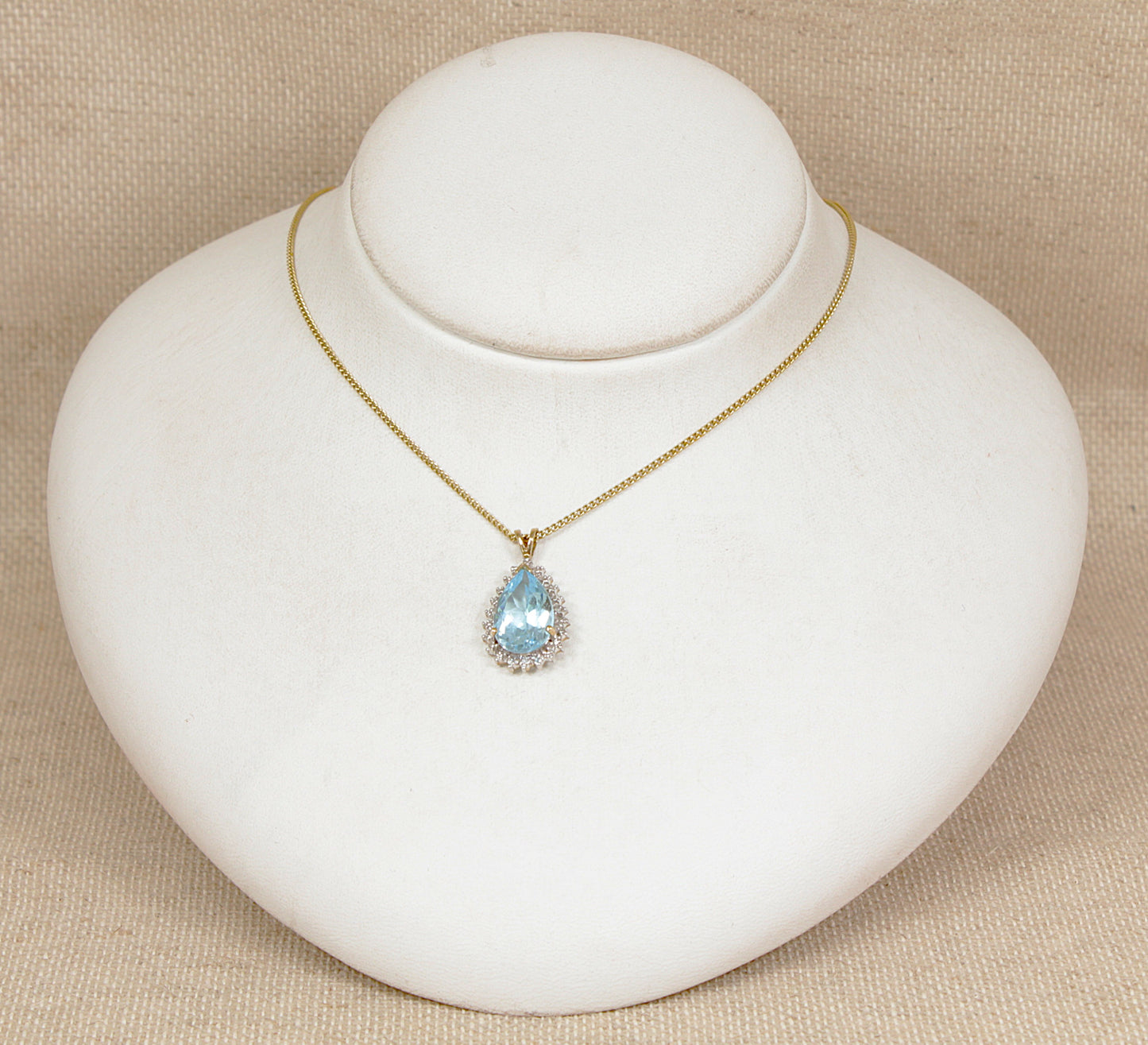 Gold necklace with a blue topaz gemstone and diamond pendant on a white jewelry display.