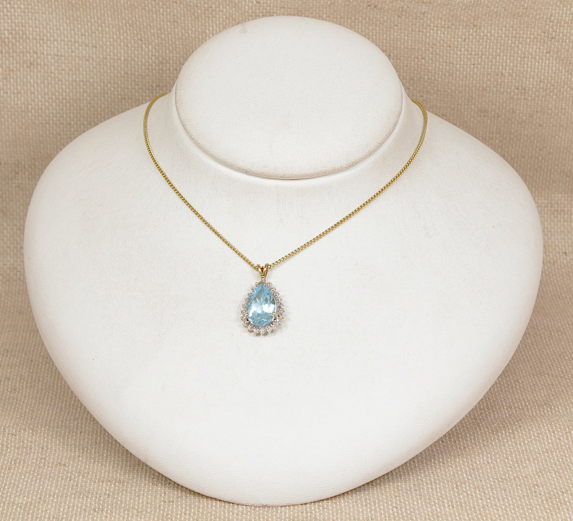 Gold necklace with a blue topaz gemstone and diamond pendant on a white jewelry display.