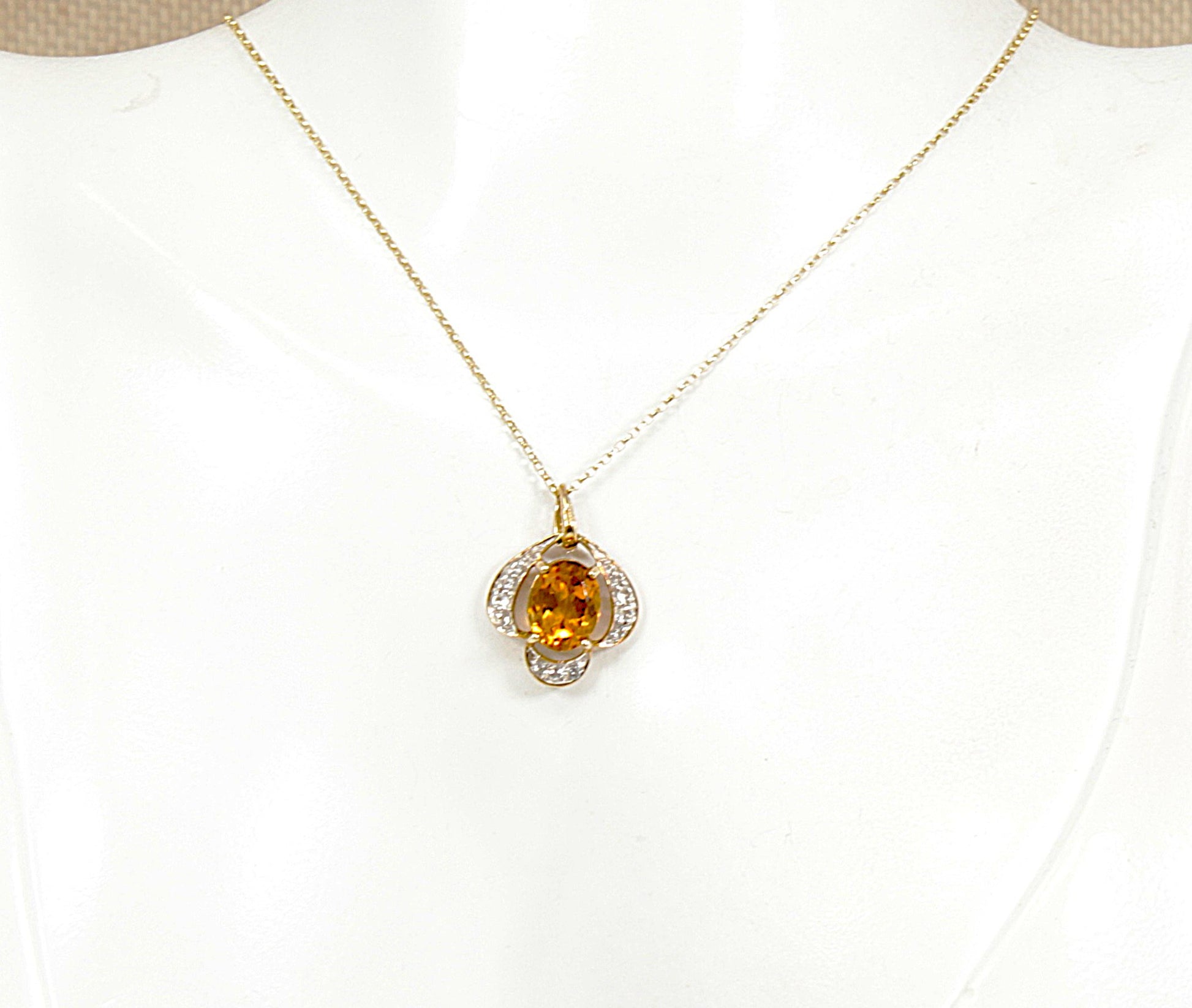 A gold chain necklace with a flower-shaped pendant featuring a central round citrine gemstone and small clear white citrine accent gemstones, displayed on a white jewelry bust.