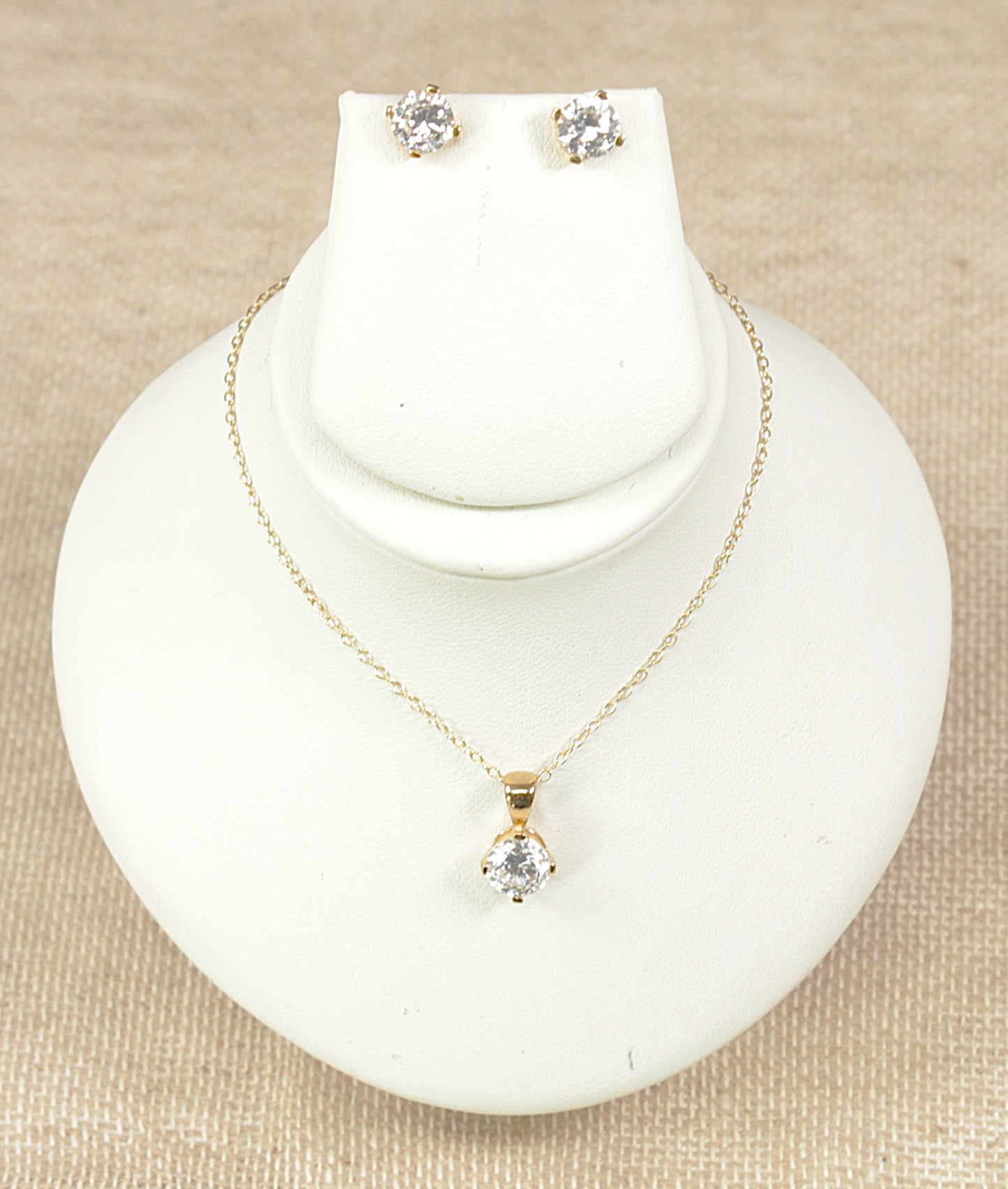 Gold pendant necklace and gold earrings jewellery set on a white display bust.
