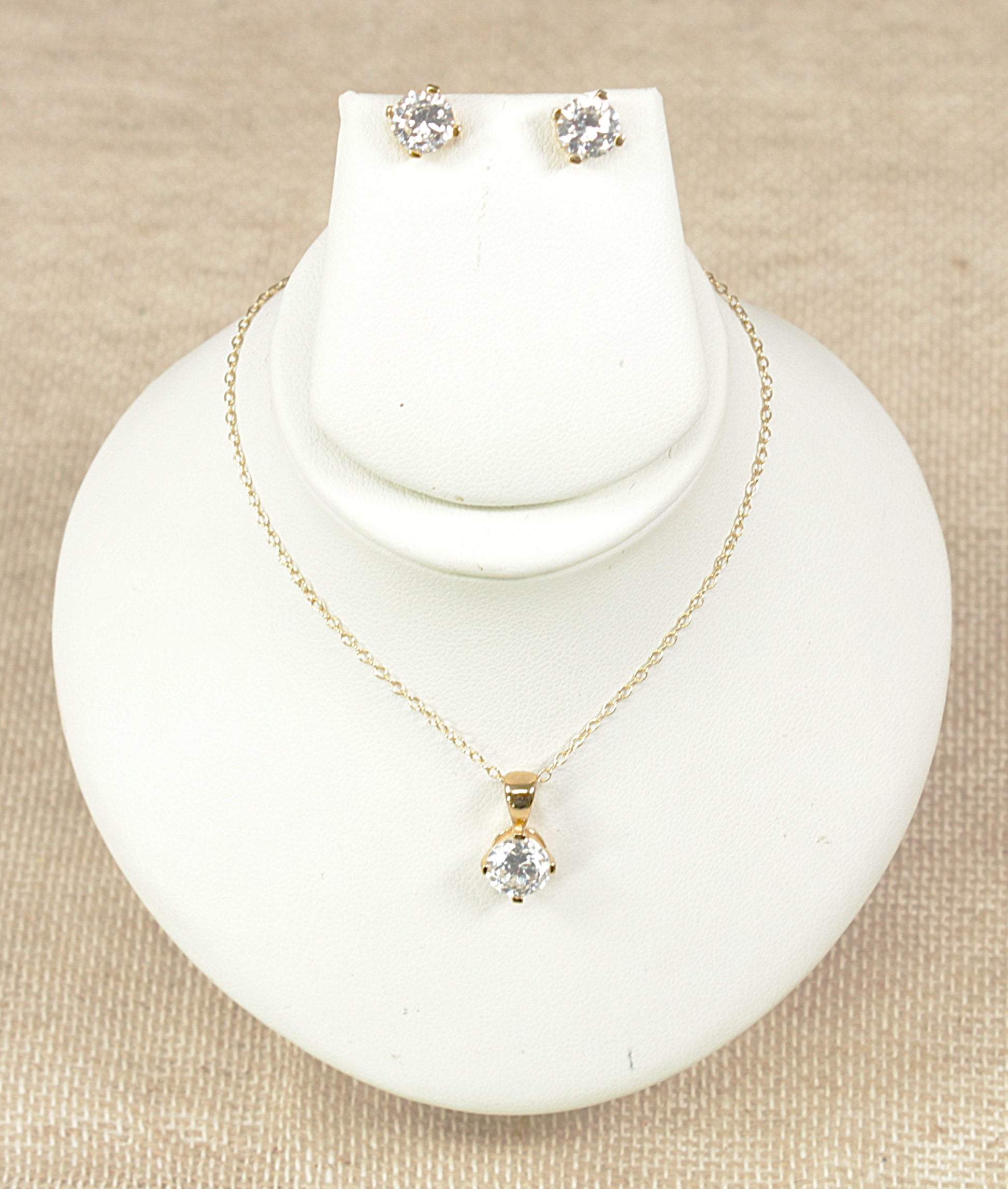 Gold pendant necklace and gold earrings jewellery set on a white display bust.