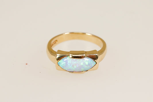 A 9ct gold ring with an opal centerpiece set in an ellipse bezel, displaying vibrant orange, red, and yellow hues against a white background. 