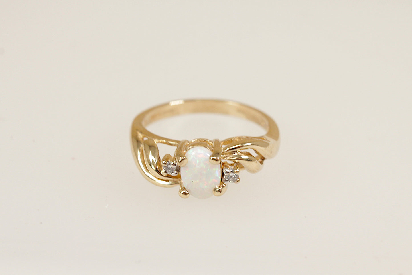An elegant 9ct yellow Gold ring showcasing a vibrant oval-cut fire Opal, securely held in a classic four-claw crown setting. On either side of the opal, a sparkling round-cut diamond is set asymmetrically, adding a modern, artistic touch to the design. UK finger size N.