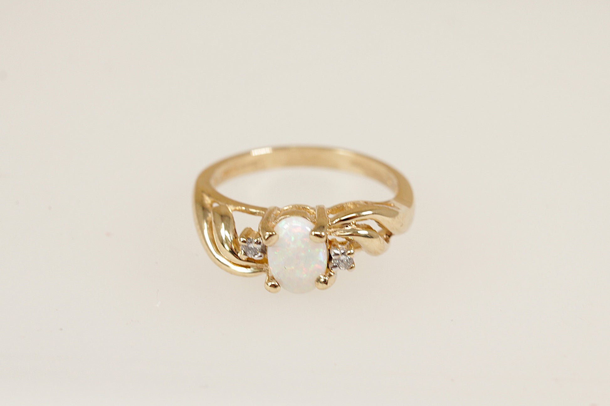 An elegant 9ct yellow Gold ring showcasing a vibrant oval-cut fire Opal, securely held in a classic four-claw crown setting. On either side of the opal, a sparkling round-cut diamond is set asymmetrically, adding a modern, artistic touch to the design. UK finger size N.