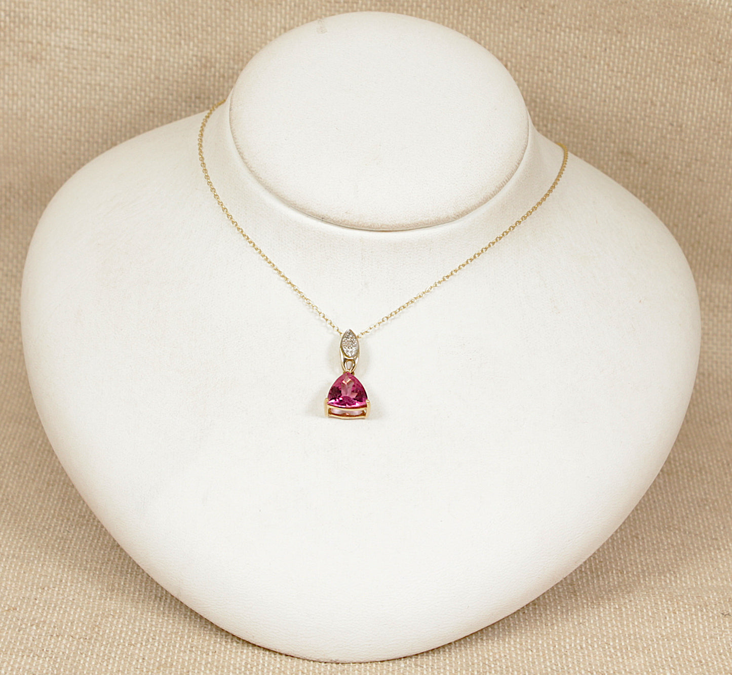 Gold necklace with a heart-shaped pink tourmaline and diamond gemstones pendant on a white stand.
