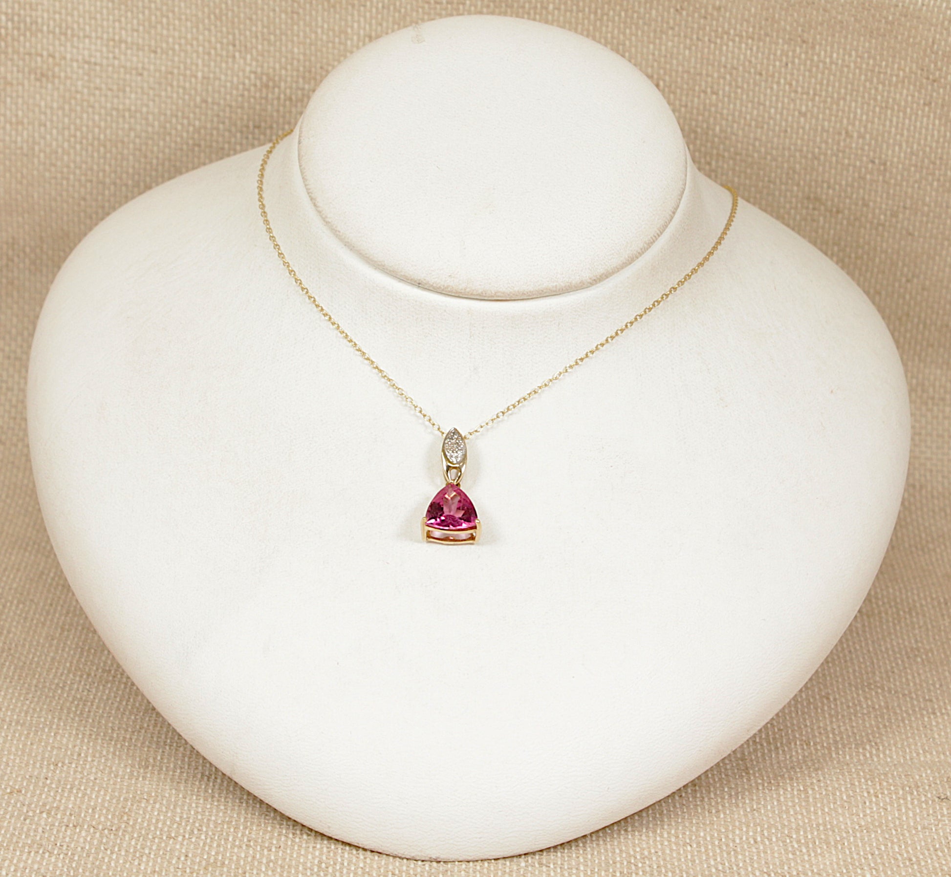 Gold necklace with a heart-shaped pink tourmaline and diamond gemstones pendant on a white stand.