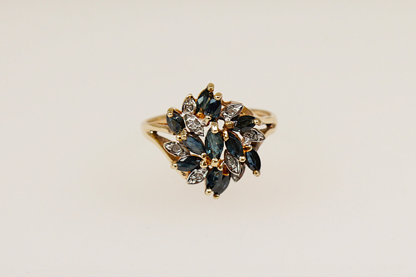 This 9ct Gold ring is a breathtaking and artistic statement piece! This large Sapphire and Diamond flower design ring features 11 Marquise-cut blue Sapphires in claw settings and 8 round diamond accents, Birmingham hallmarks for year 1994 and stamped DIA. UK finger size O. 