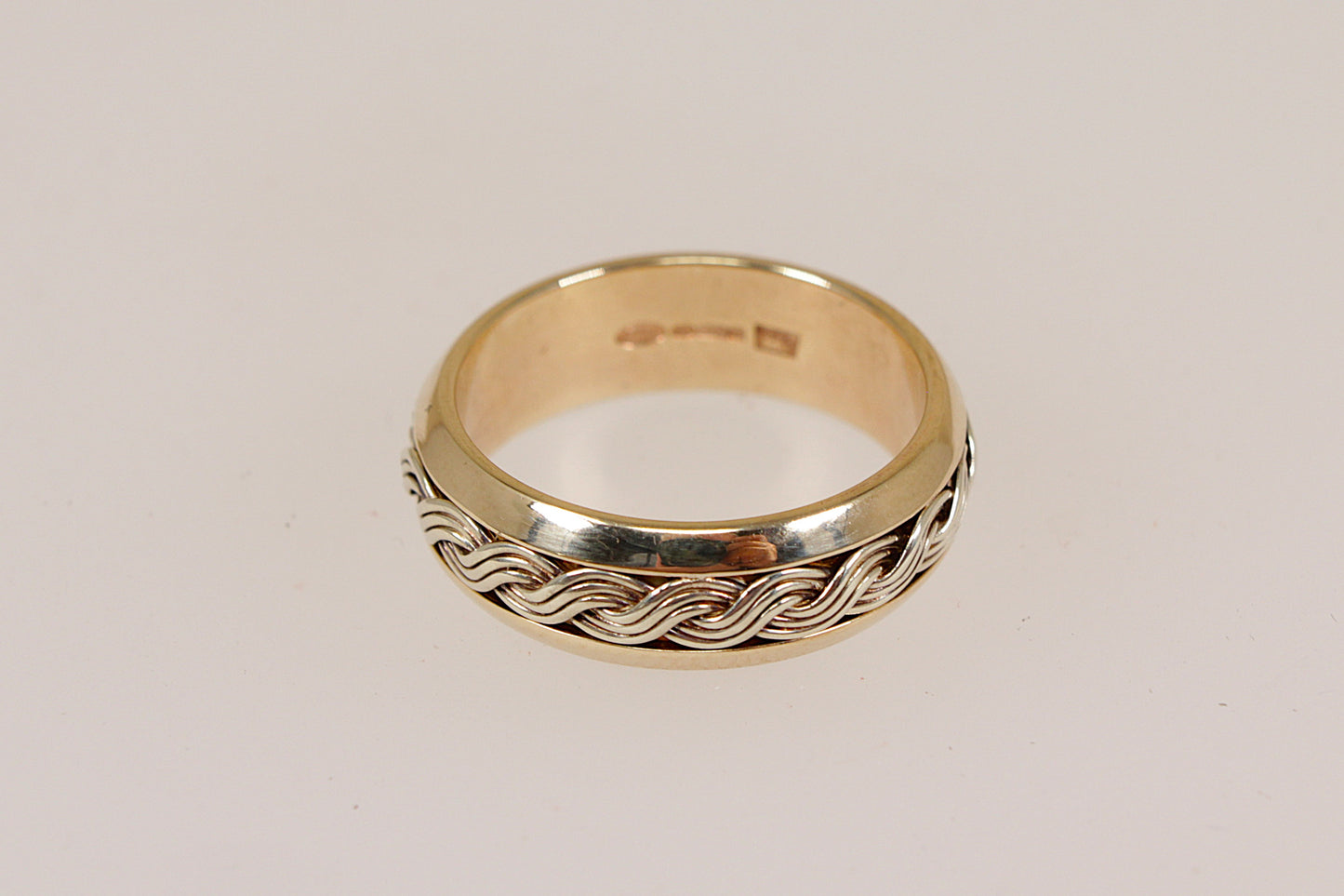 Gold ring with braided woven lives design on a light gray background