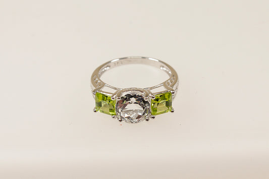 A 9ct white gold trilogy ring with a round white topaz centerpiece and square-cut peridot side stones on a white background.