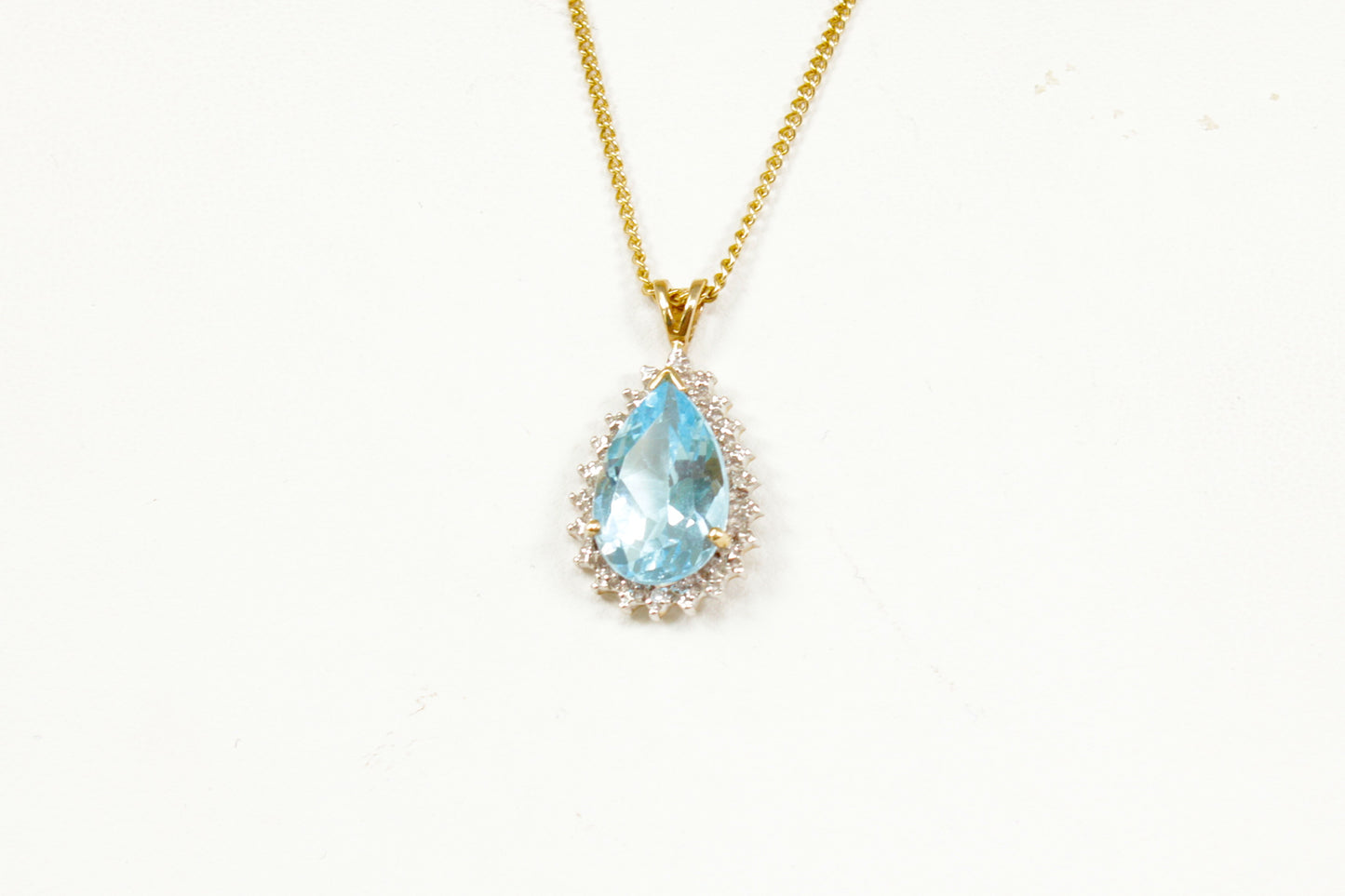 Gold necklace with a blue teardrop topaz pendant on a white background
