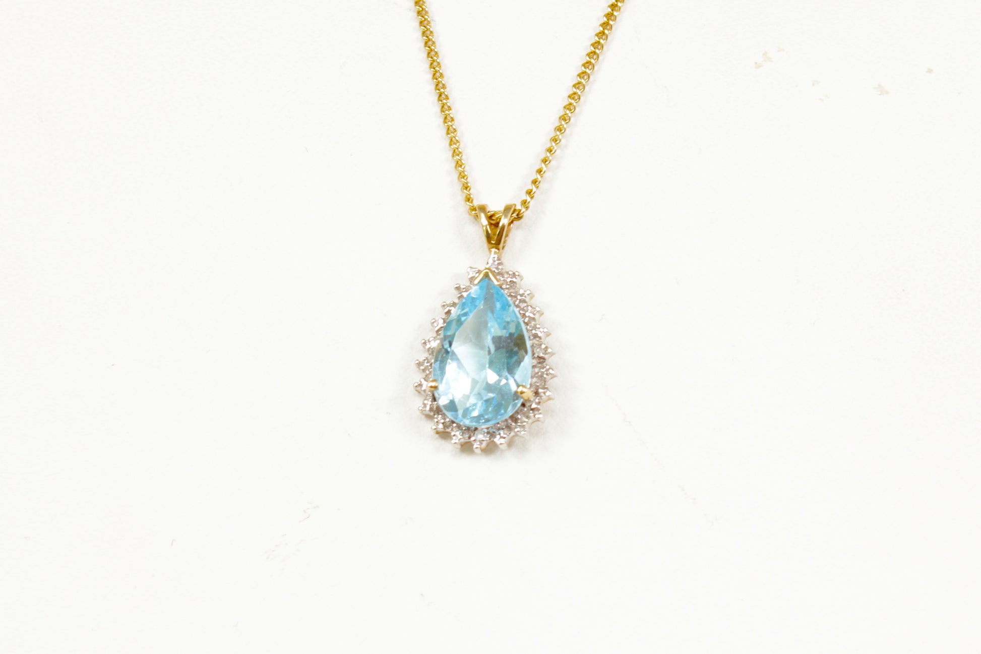 Gold necklace with a blue teardrop topaz pendant on a white background