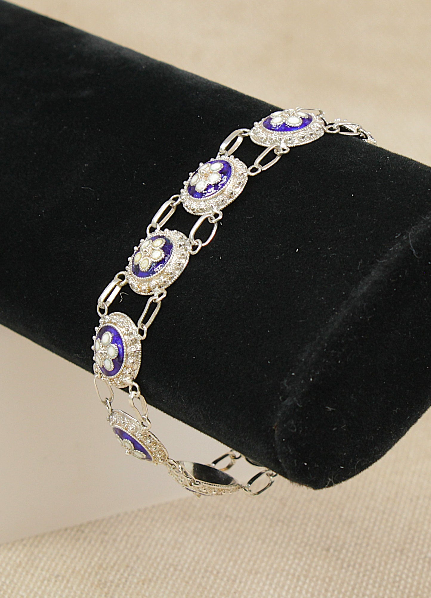 Silver bracelet with blue enamel flowers a black velvet stand