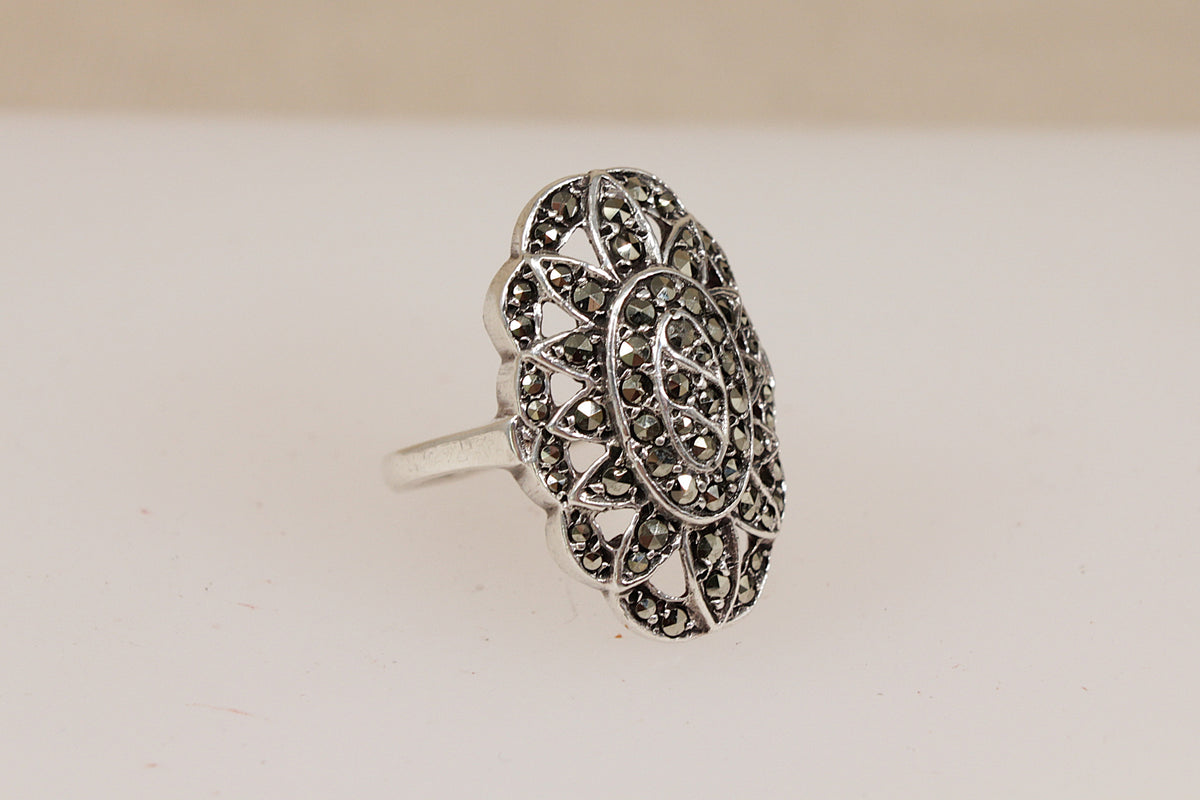 A vintage silver ring with an intricate, openwork floral or medallion design set with small marcasite gemstones, shown on a plain light background.
