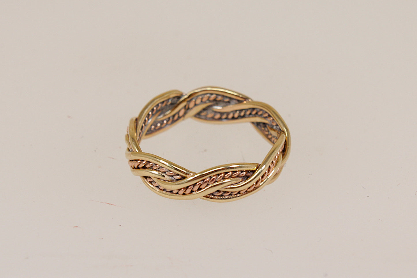 A twisted rope-style band ring in yellow gold with textured rose gold recessed detailing, photographed on a plain off-white background.
