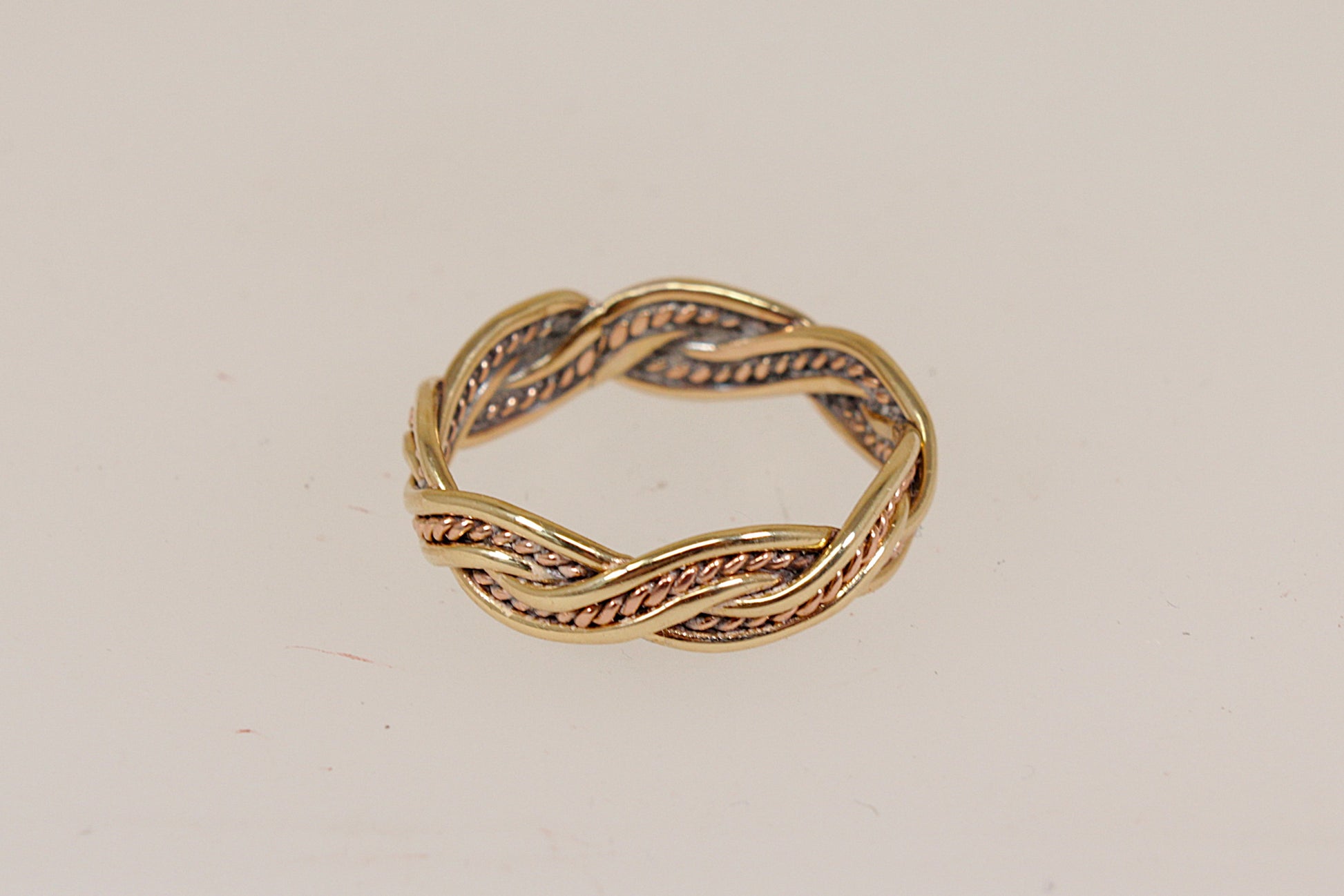 A twisted rope-style band ring in yellow gold with textured rose gold recessed detailing, photographed on a plain off-white background.