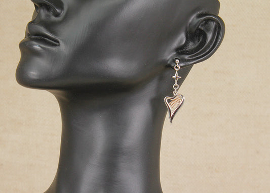 A Clogau silver and gold dangle earring in the shape of a harp with a small cross  charm, shown on a black mannequin head against a beige background.