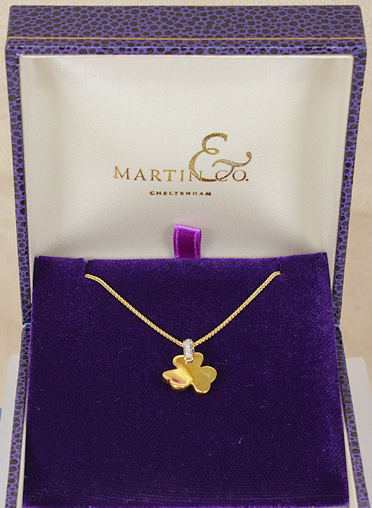 A gold clover pendant necklace on a gold chain, presented in an open purple velvet jewelry box with a white inner lid printed with the Martin & Co. brand name.