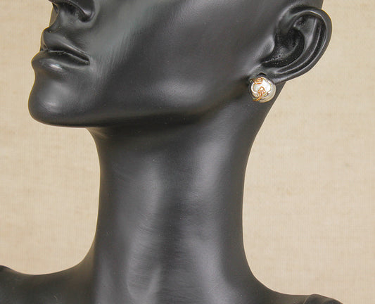 A close-up of a black mannequin bust wearing a small silver gold Clogau art nouveau style mother of pearl stud earring against a light beige background.