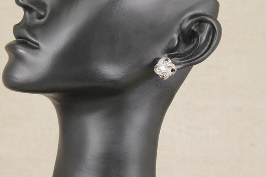 A close-up of a black mannequin head and neck wearing a small sterling silver stud earring with a clear crystal gemstone, against a light beige background.