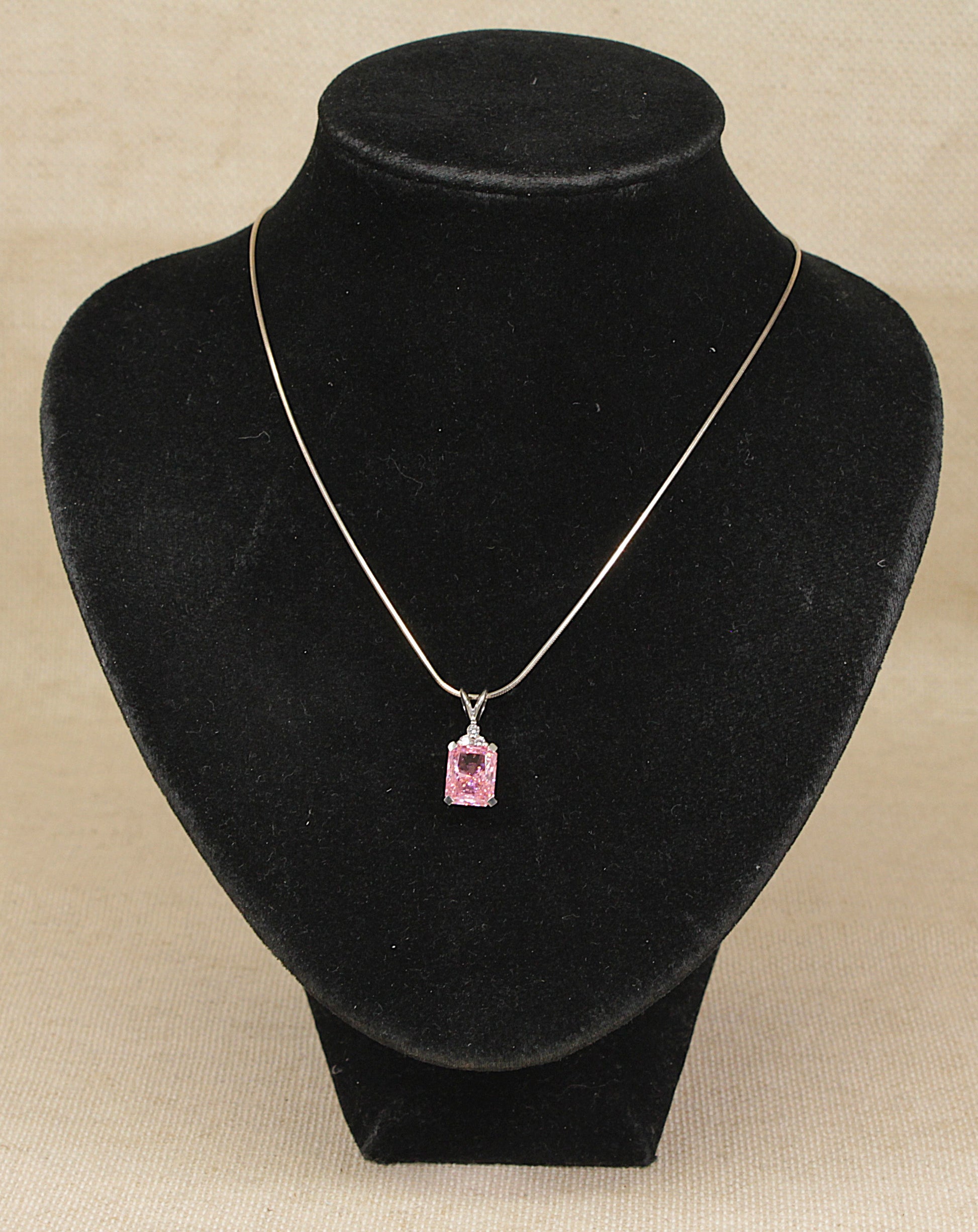 A sterling silver necklace with a rectangular pink gemstone pendant, displayed on a black necklace bust against a beige background.