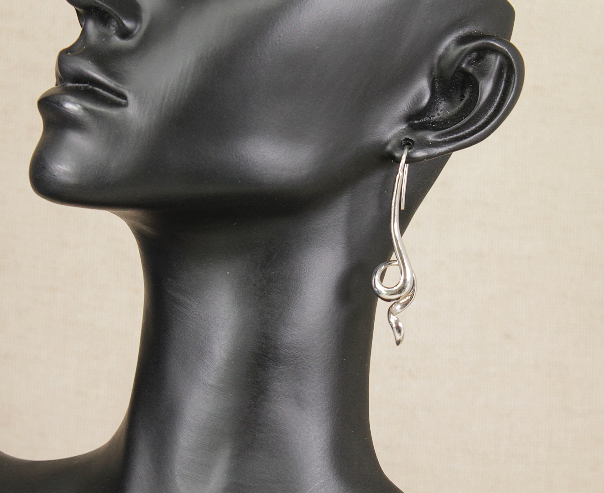 Silver drop earring on a black mannequin head against a beige background