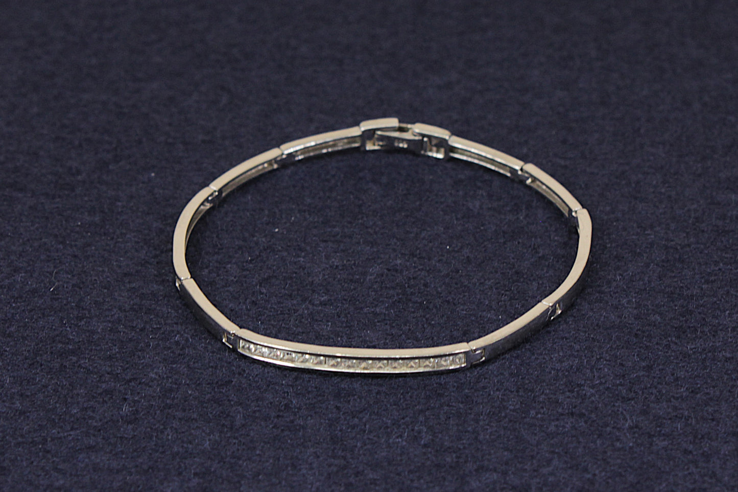 A silver-toned segmented bangle bracelet with a row of small clear stones along the front, displayed on a dark textured background.