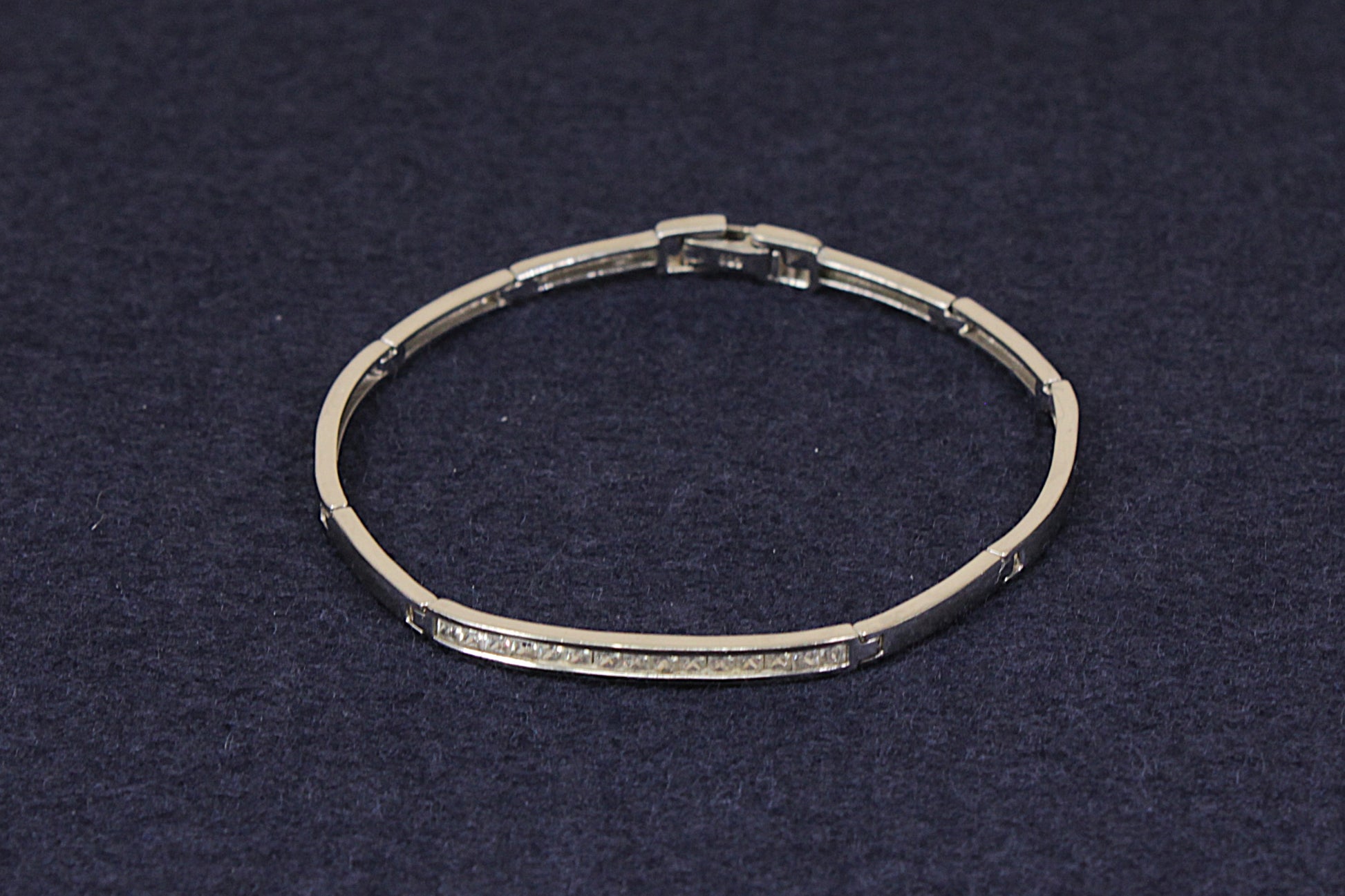 A silver-toned segmented bangle bracelet with a row of small clear stones along the front, displayed on a dark textured background.