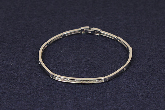 A silver-toned segmented bangle bracelet with a row of small clear stones along the front, displayed on a dark textured background.