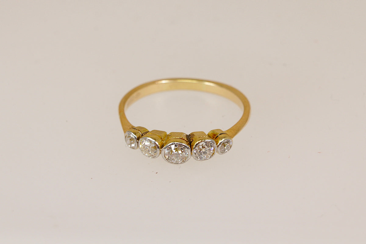 An 18ct yellow gold ring featuring five round-cut clear diamond gemstones set in a row on the band, photographed against a plain off-white background.