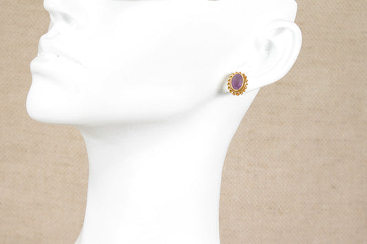 A single 9ct gold stud earring with an oval purple amethyst gemstone, displayed on a white mannequin head against a beige textured background.